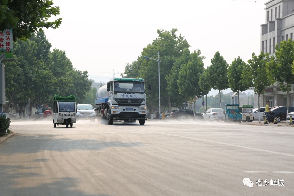 2019 年峄城街景:绿树之间,环卫洒水车与日常车辆经过街道